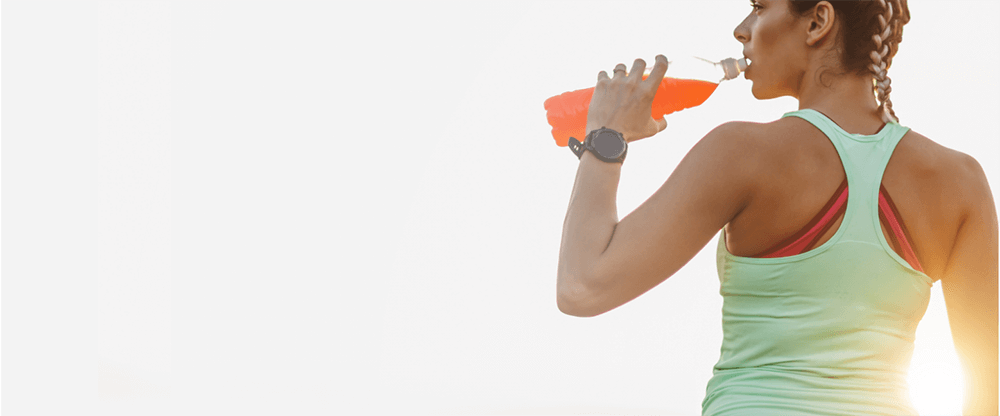 Photo of a female athlete drinking out of a plastic water bottle that is filled with orange liquid
