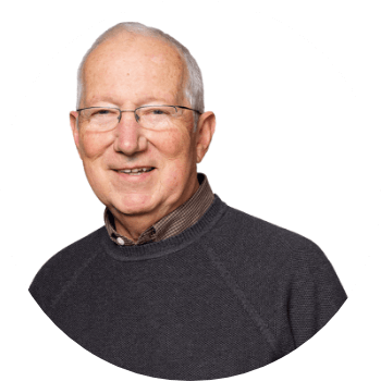 Photo of a man smiling and wearing a grey sweater over a brown dress shirt