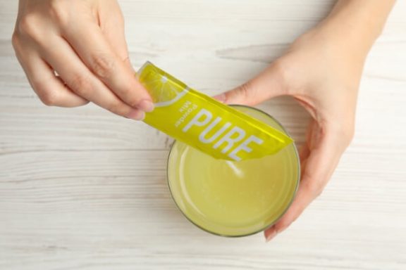 Photo of someone dumping a lemon packet of powder mix into a beverage