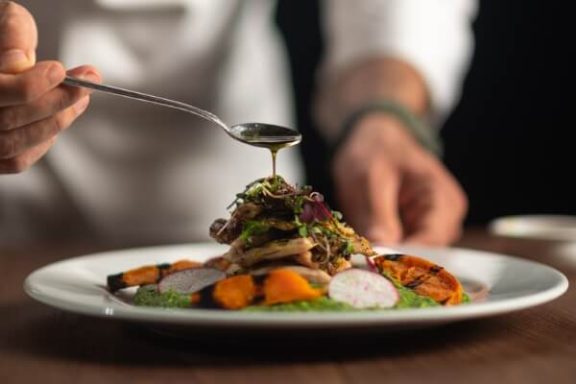 Close up photo of food on a plate while someone uses a spoon to pour sauce on top