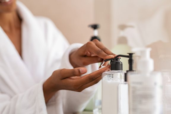Photo of a woman wearing a white robe using a lotion pump to get lotion on her hand