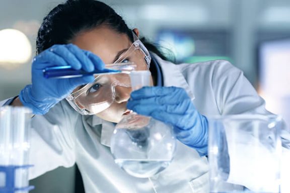 Photo of a woman in a lab coat pouring liquid into a beaker